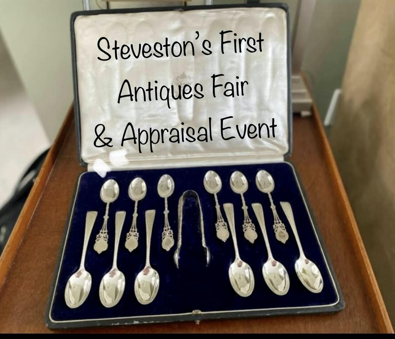 A set of silver spoons in a velvet case is on display with the words "Steveston's First Antique Fair and Appraisal Event"